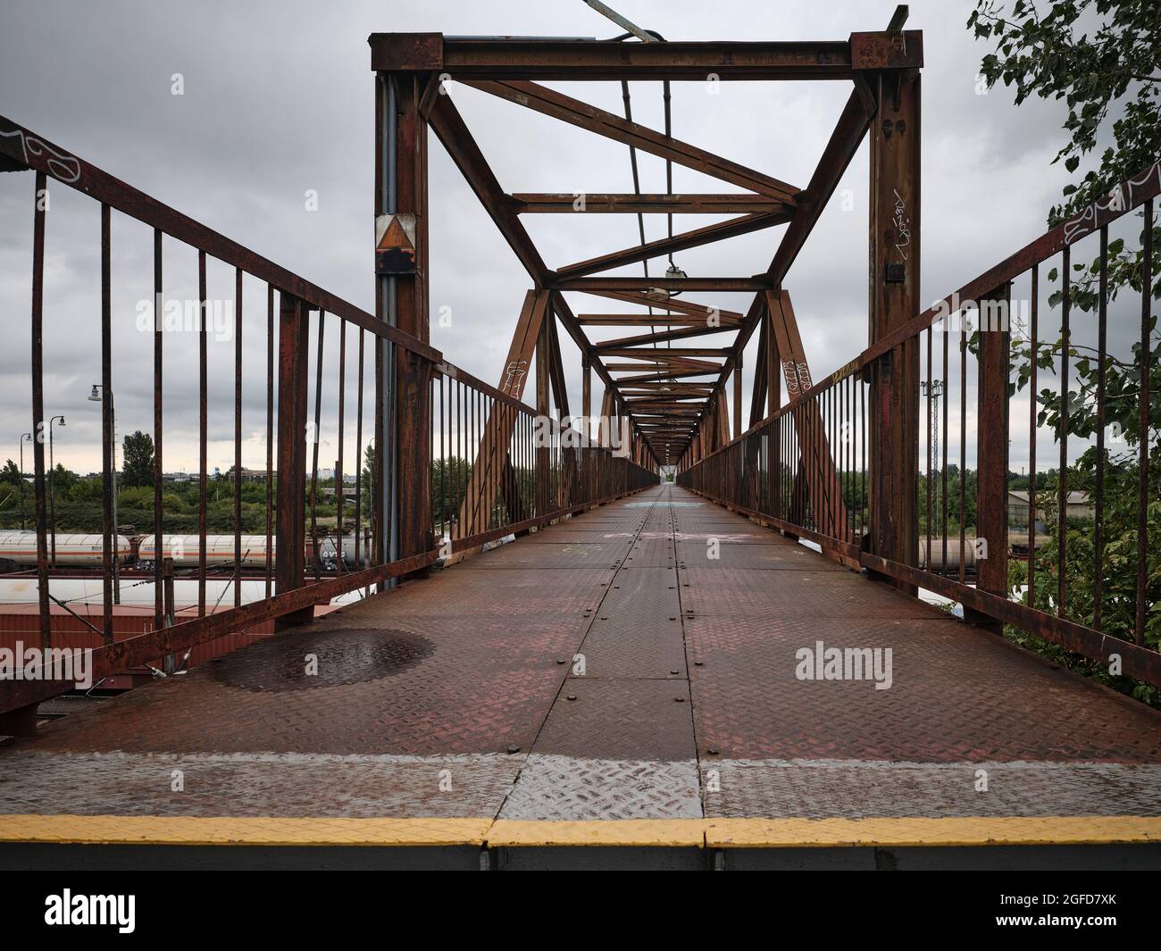 Ponte pedonale in ferro arrugginito con forti linee guida e prospettiva industriale sotto un cielo nuvoloso. Foto Stock