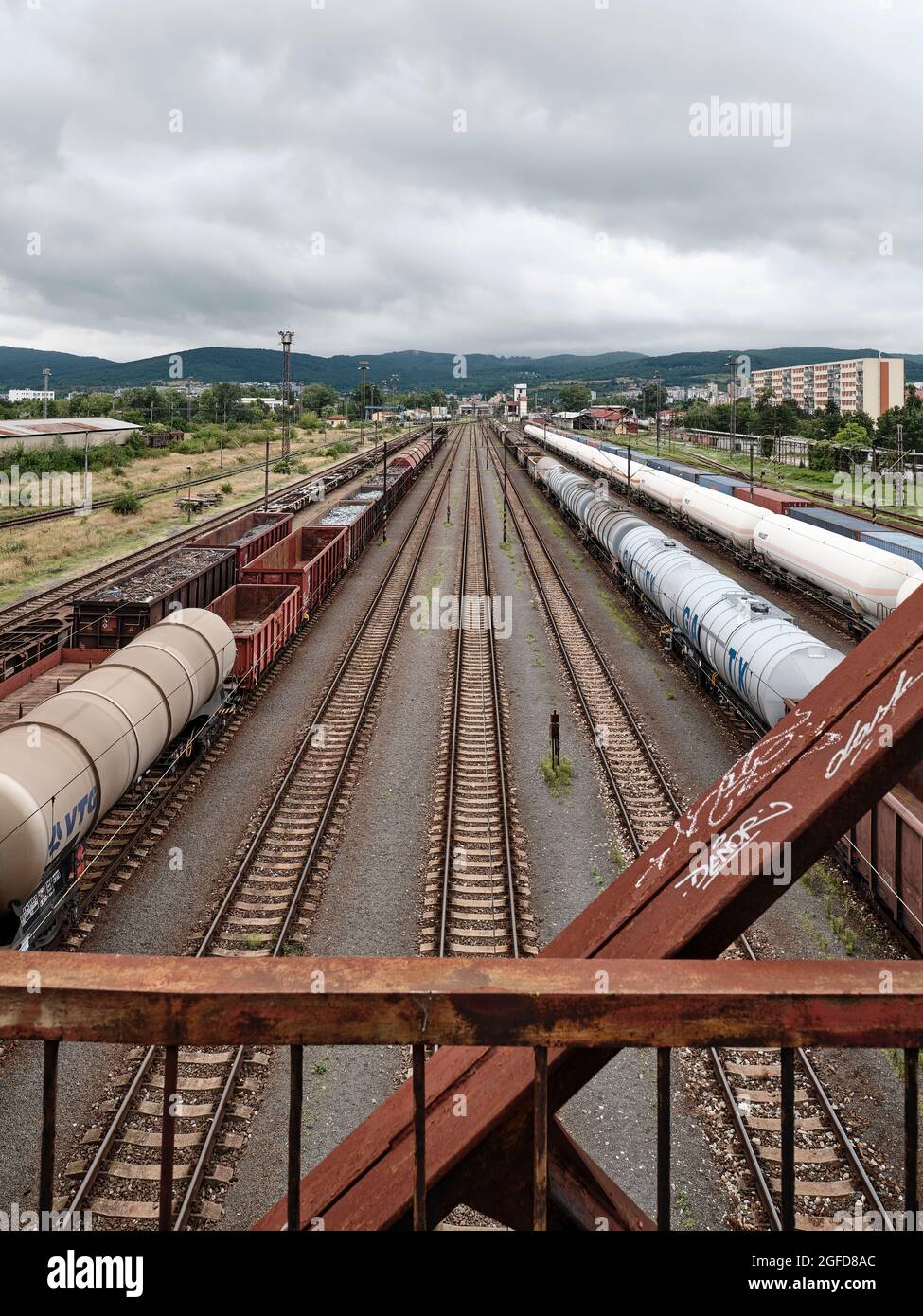 Treni merci e binari ferroviari in un grande deposito ferroviario visto da un ponte arrugginito sotto il cielo nuvoloso Foto Stock