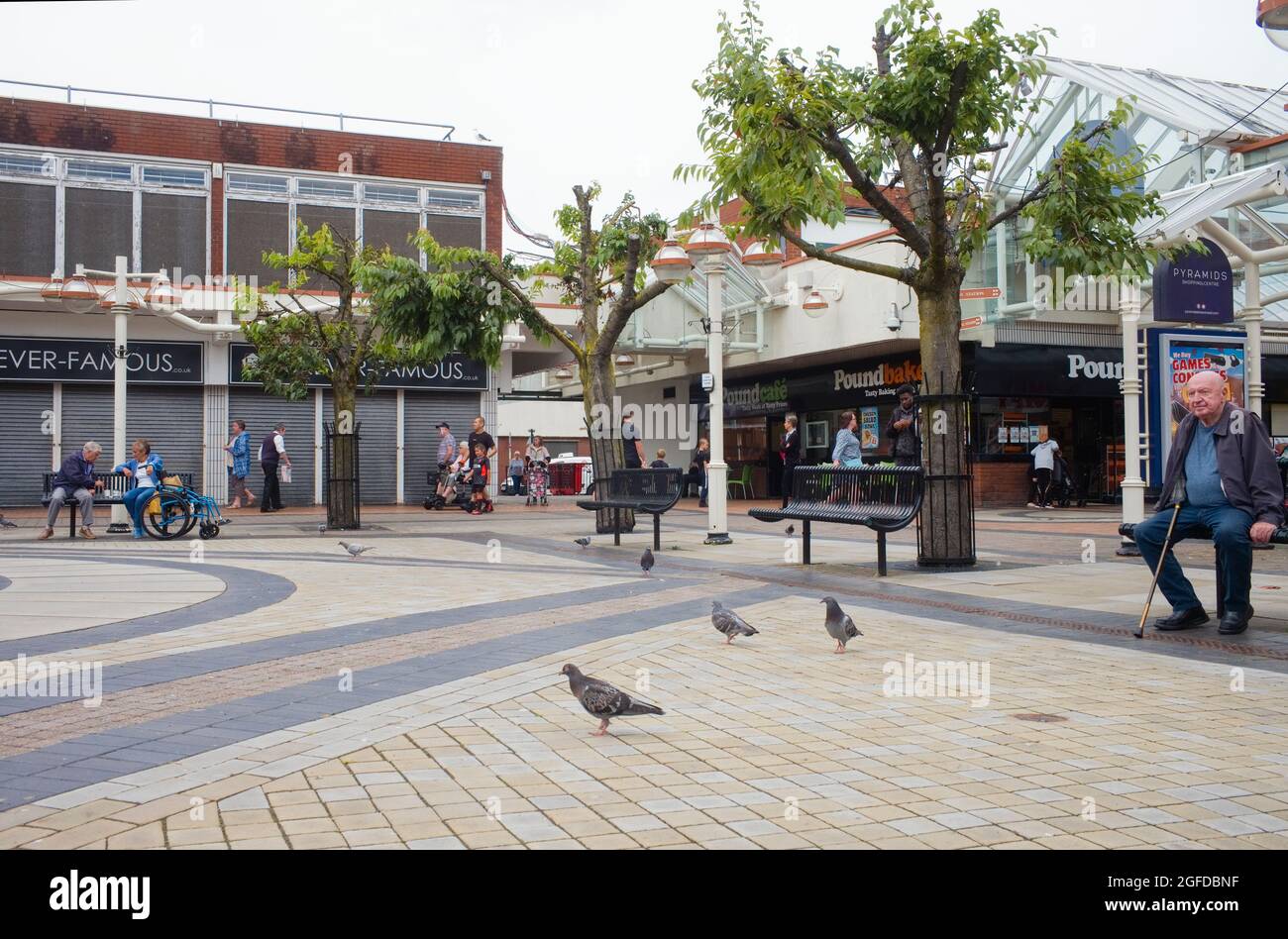 Uomo anziano seduto sul banco al centro commerciale Run Down Pyramids a Birkenhead, Merseyside Foto Stock