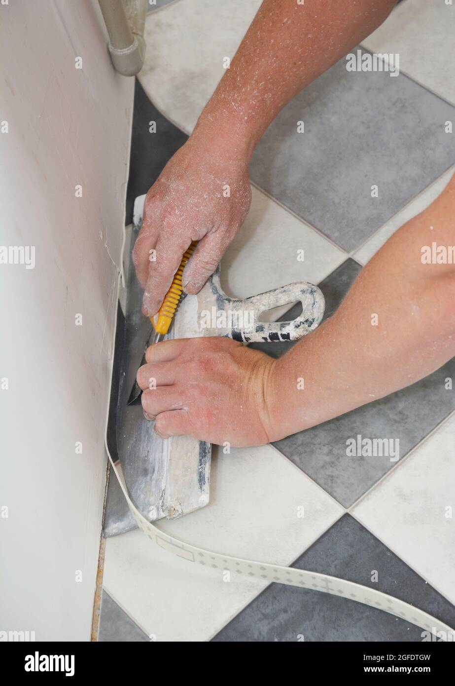 Un artigiano sta installando pavimenti in linoleum vinile e sta tagliando, rifilando i bordi di un foglio in vinile e linoleum lungo la parete con un coltello per stucco largo Foto Stock