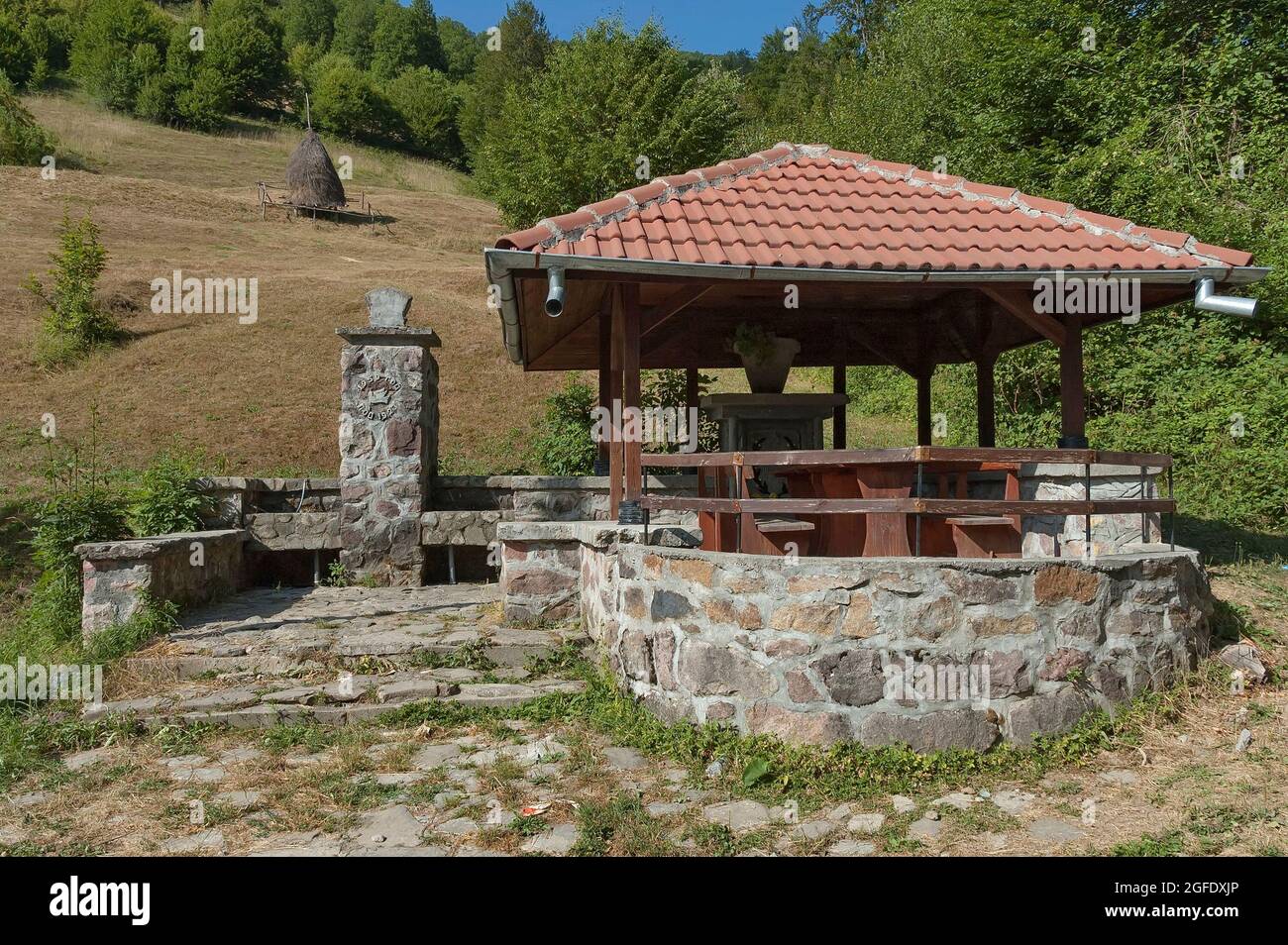 Vista su un pascolo di montagna con tradizionali mucchi di fieno per l'inverno e una casa estiva con una fontana costruita su uno spartiacque da soldati Foto Stock