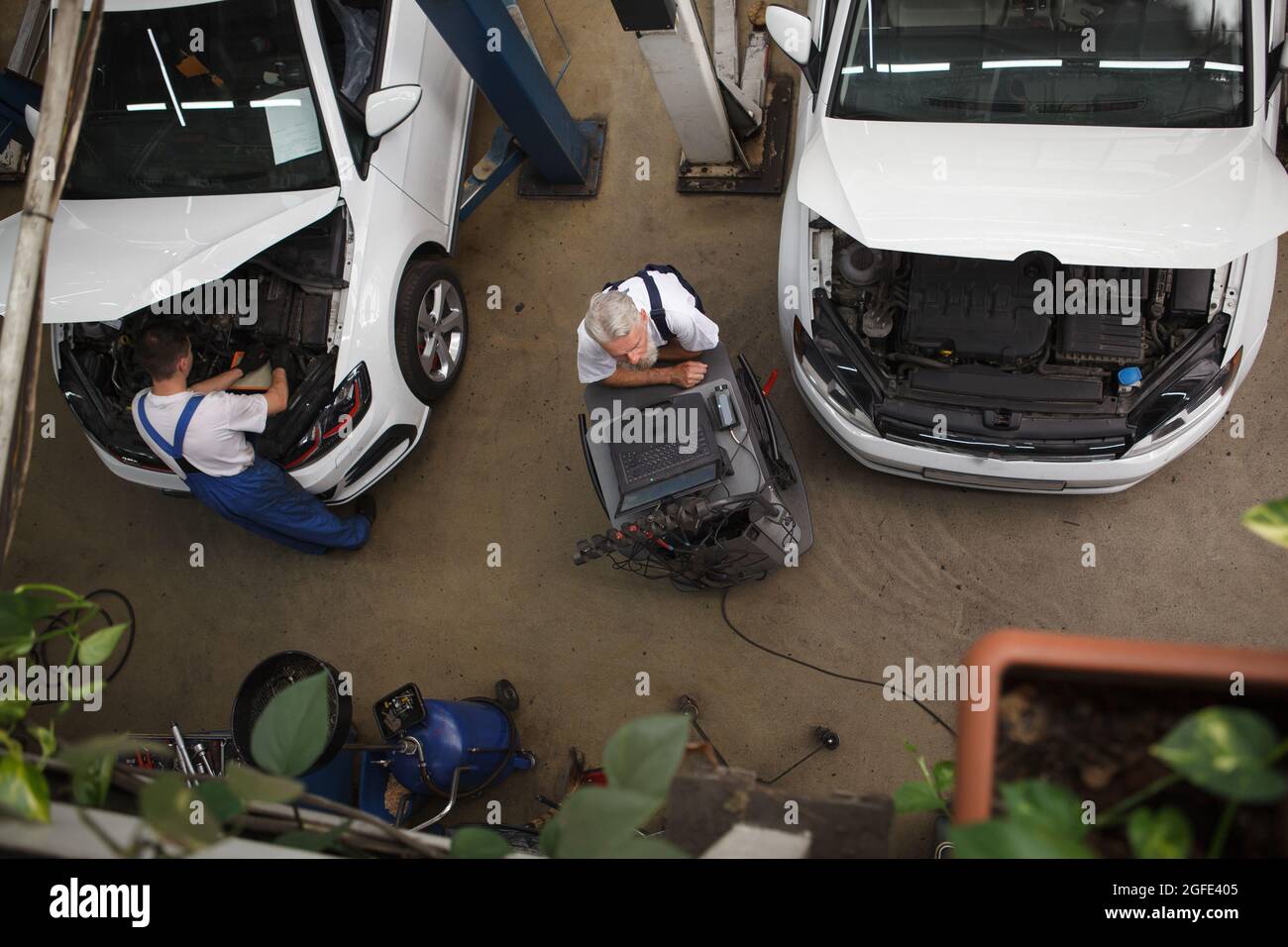 Immagine dall'alto di un meccanico tra due vetture con cappe aperte in officina Foto Stock