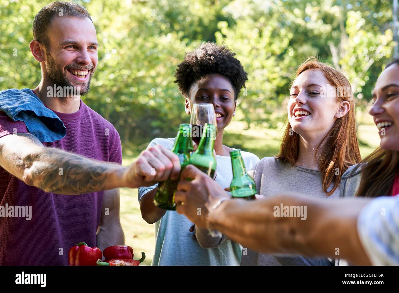 Giovani amici felici che tostano bottiglie di birra in giardino Foto Stock