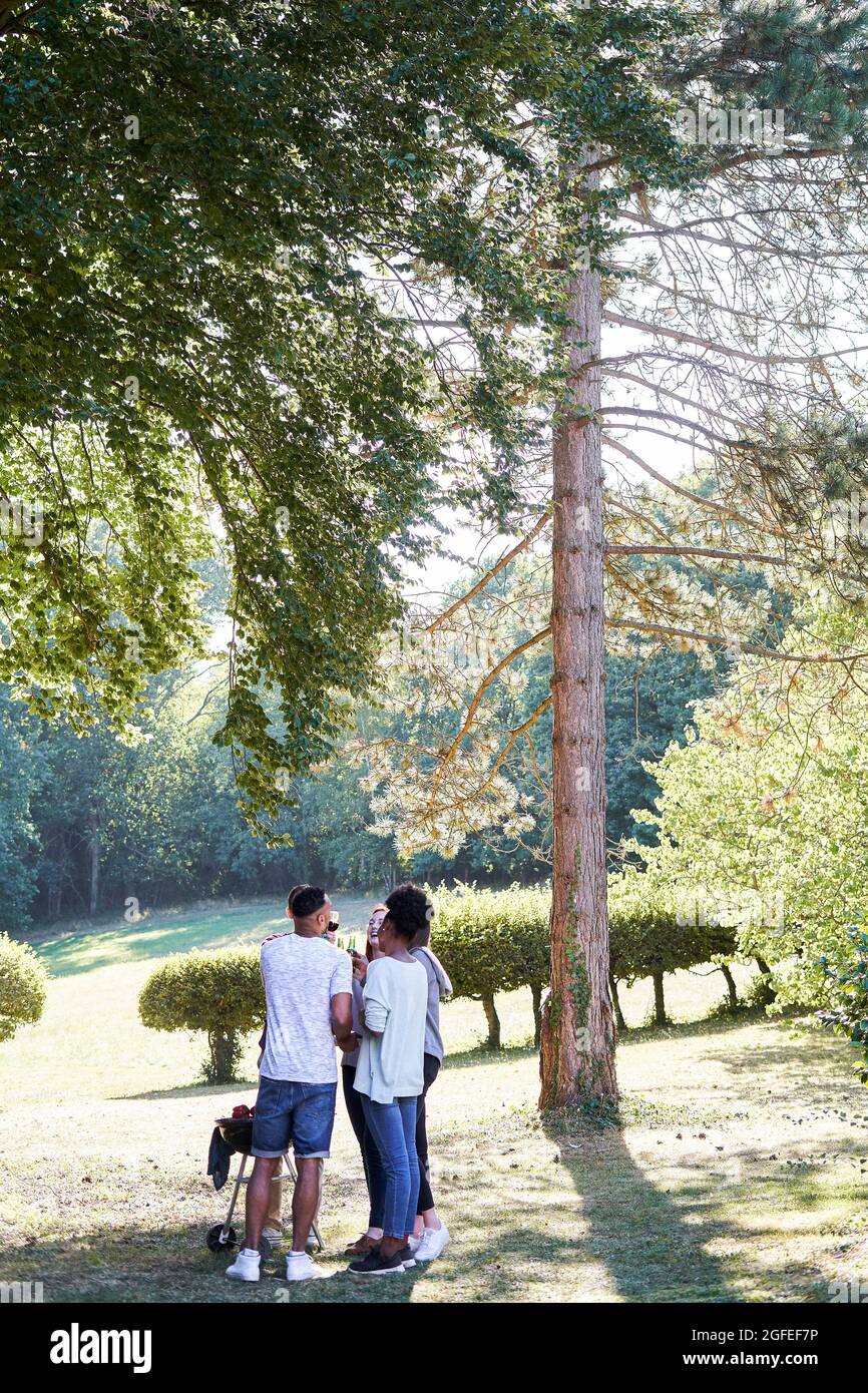 Giovani amici felici che tostano bottiglie di birra in giardino Foto Stock