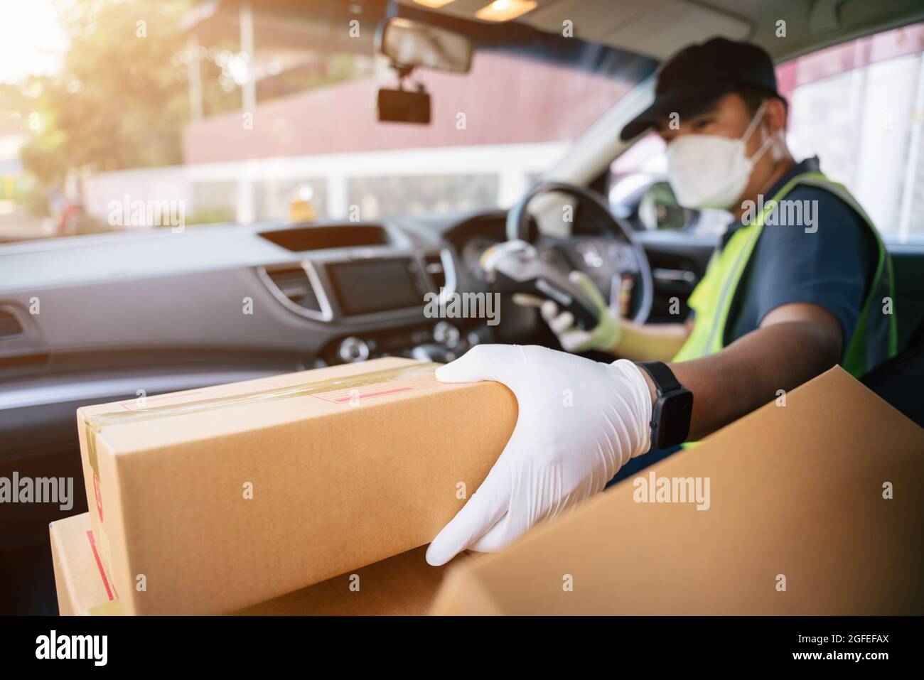 Un addetto alla consegna che detiene il lettore di carte di credito sta raccogliendo una scatola in auto di un amico per consegnarla a un cliente, selezionare fuoco una scatola. Foto Stock