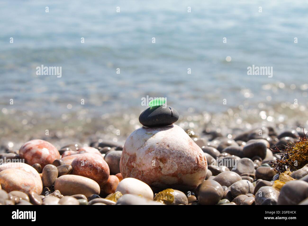 La piramide è costruita su una spiaggia di ciottoli di mare con un vetro verde satinato liscio in cima. Sullo sfondo di onde, schizzi d'acqua e. Foto Stock