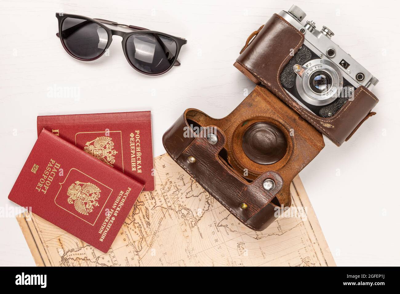 Mappa del mondo, due passaporti, una vecchia macchina fotografica in una custodia di pelle e occhiali da sole su un tavolo di legno bianco. Vista da above.inscription - passaporto russo Foto Stock
