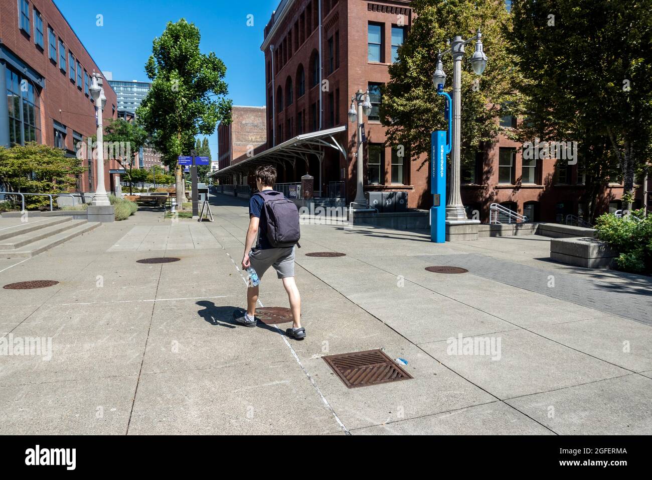 Tacoma, WA USA - circa agosto 2021: Giovane uomo con uno zaino che cammina attraverso il campus dell'Università di Washington in una giornata di sole. Foto Stock