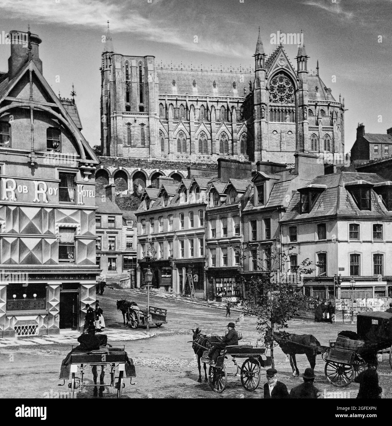Una fotografia dei primi anni del XX secolo di veicoli trainati da cavalli e conducenti vicino al porto di Cobh, County Cork, Irlanda. Sopra di loro si innamora la chiesa cattedrale ancora incompiuta di San Colman, solitamente conosciuta come la cattedrale di Cobh. Il porto, fu chiamato 'Cove' nel 1750, ribattezzato 'Queenstown' dagli inglesi nel 1849 per commemorare una visita della Regina Vittoria, e infine cambiato in Cobh, durante la Guerra d'Indipendenza Irlandese nel 1920. Foto Stock