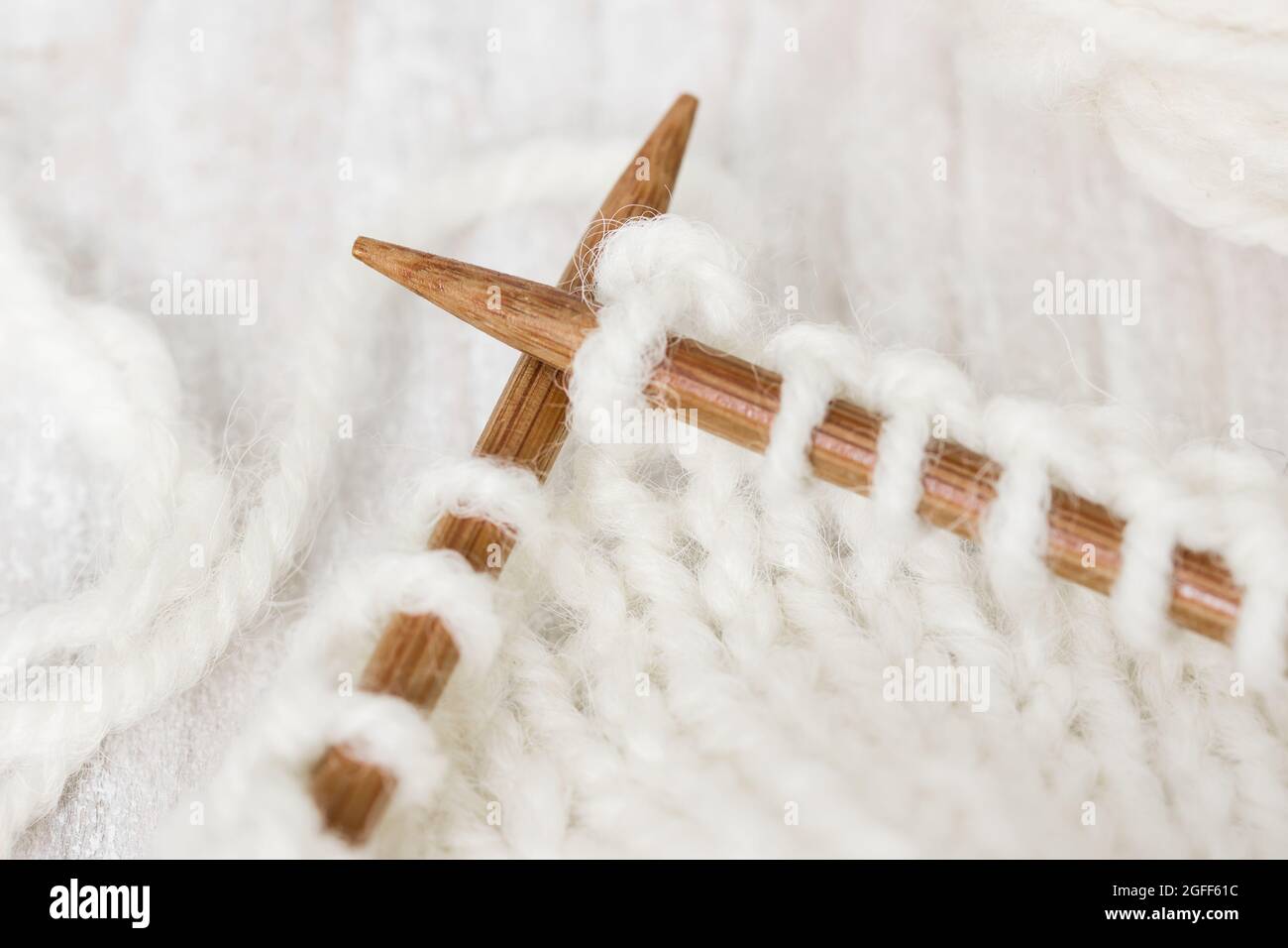 Esempio di lavorazione a maglia da filo di lana di colore bianco su aghi di legno da maglieria su sfondo ligneo. Foto Stock