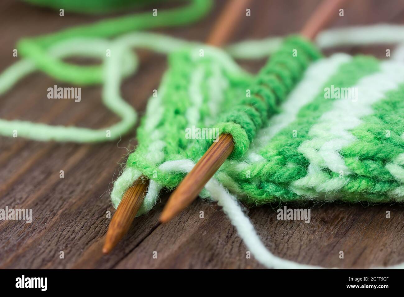 Disegno a maglia di filo verde su aghi di legno e matassa su sfondo di legno Foto Stock