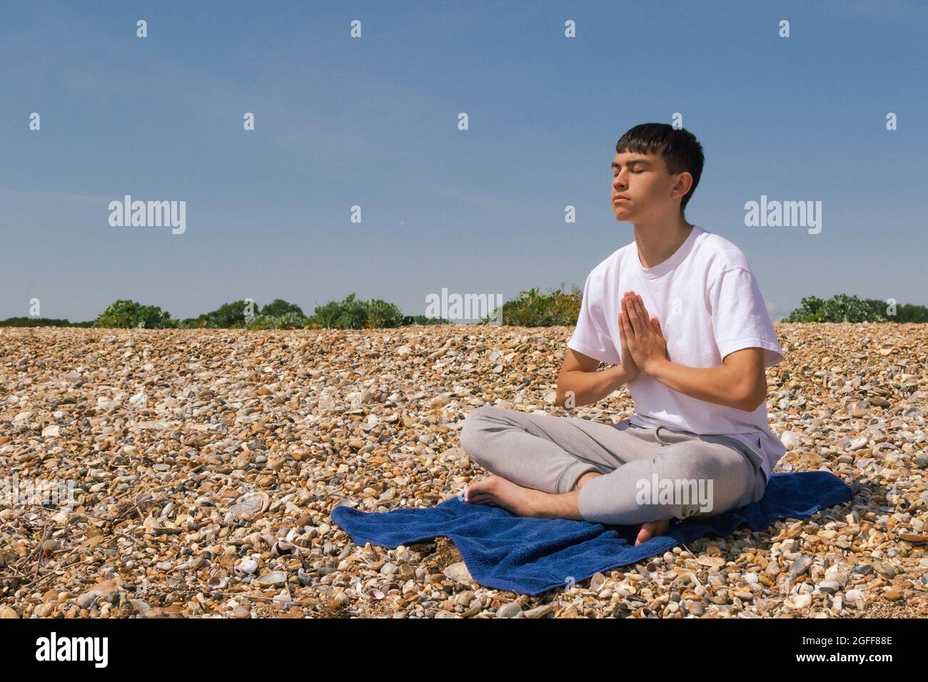 Un adolescente caucasico meditando su una spiaggia di pietra con le mani in una posizione di preghiera Foto Stock