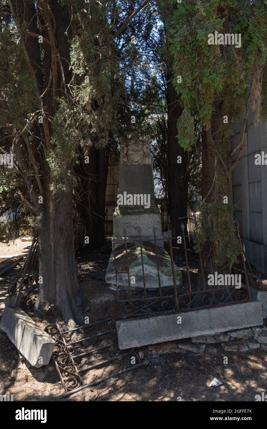 Madrid,Spagna; 6 giugno 2021: Antica tomba in cattive condizioni circondata da cipressi e con la porta in giù nella zona sacramentale del cimitero Foto Stock