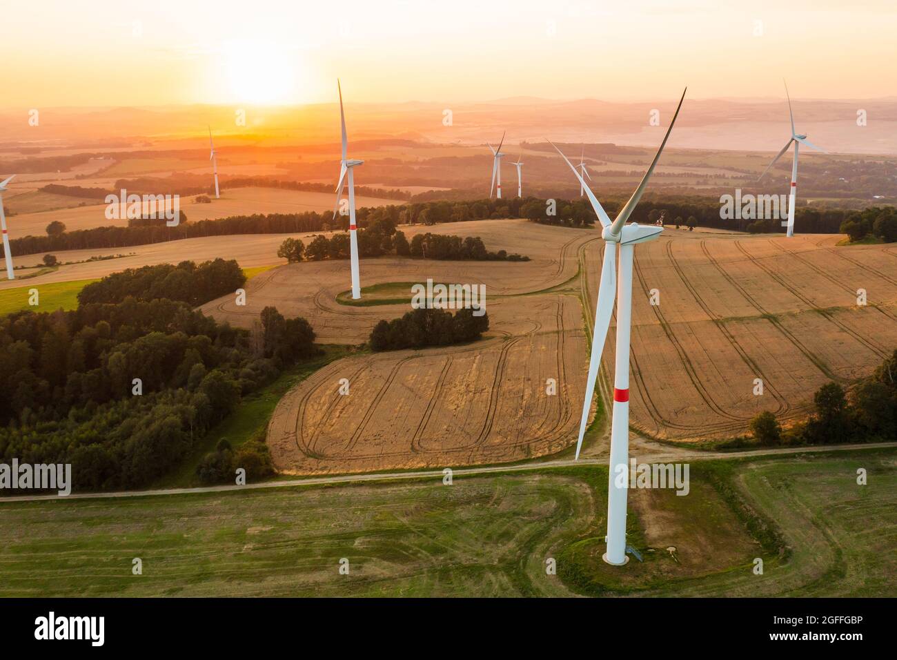 Vista panoramica di mulini a vento o turbine eoliche per la produzione di energia elettrica al tramonto sorprendente nel campo. Generazione di energia rinnovabile verde. Foto Stock