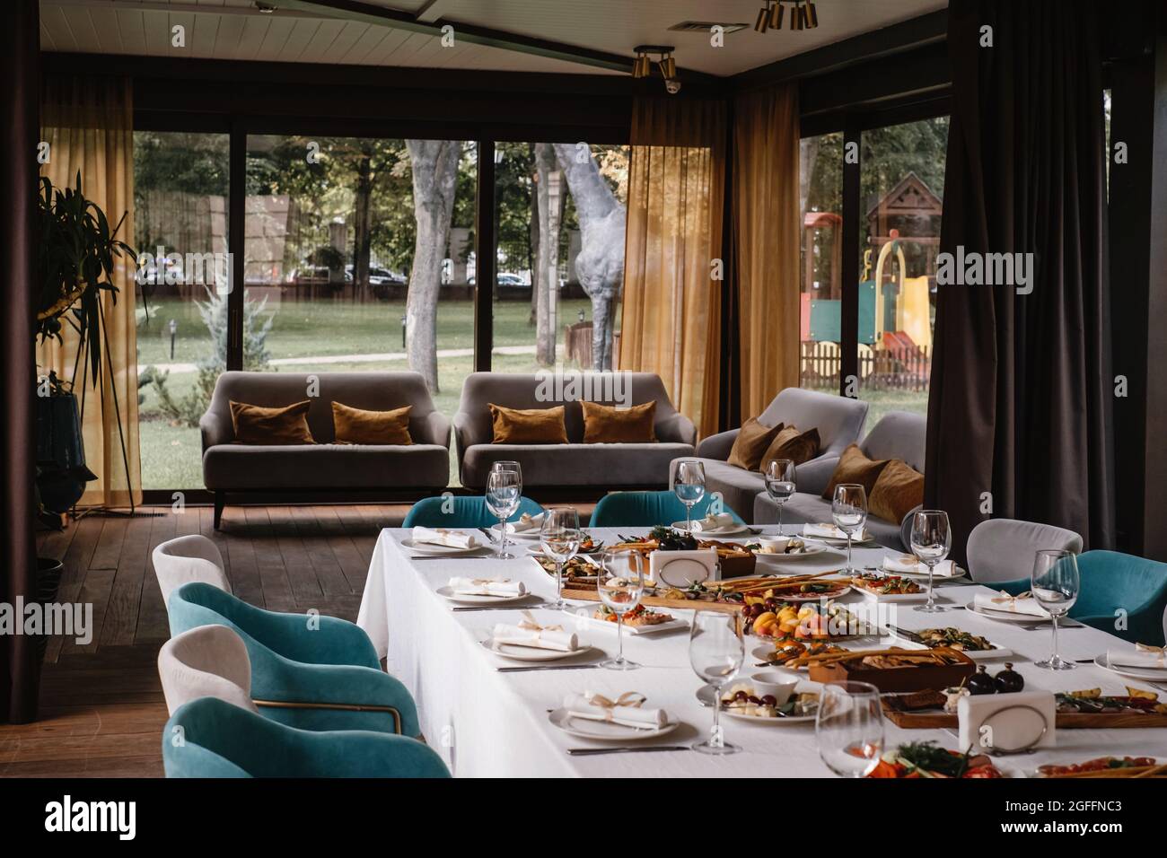 Tavolo lungo prima della celebrazione nel ristorante, bicchieri vuoti e antipasti, beg terrazza finestre. Accogliente atmosfera elegante in un ristorante di lusso Foto Stock