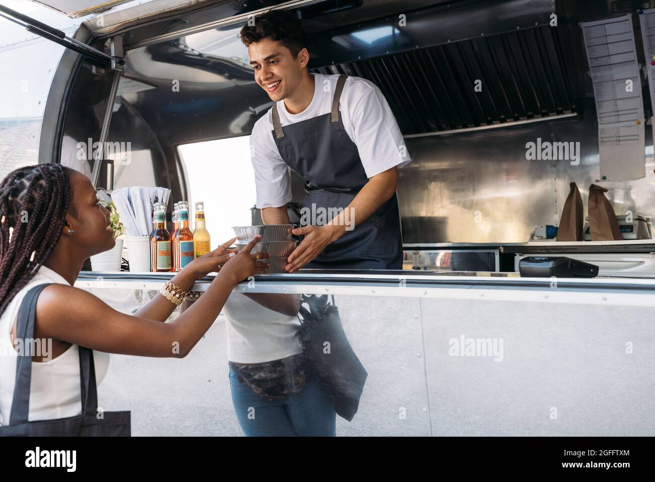 Un venditore sorridente che offre cibo confezionato da asporto a una cliente femminile. Donna che prende il cibo da un proprietario di camion del cibo. Foto Stock