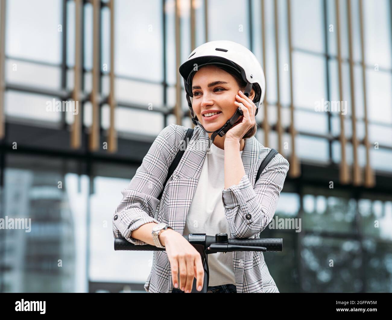 Bella donna caucasica in casco bianco appoggiato su un manubrio di scooter elettrico push guardando via Foto Stock