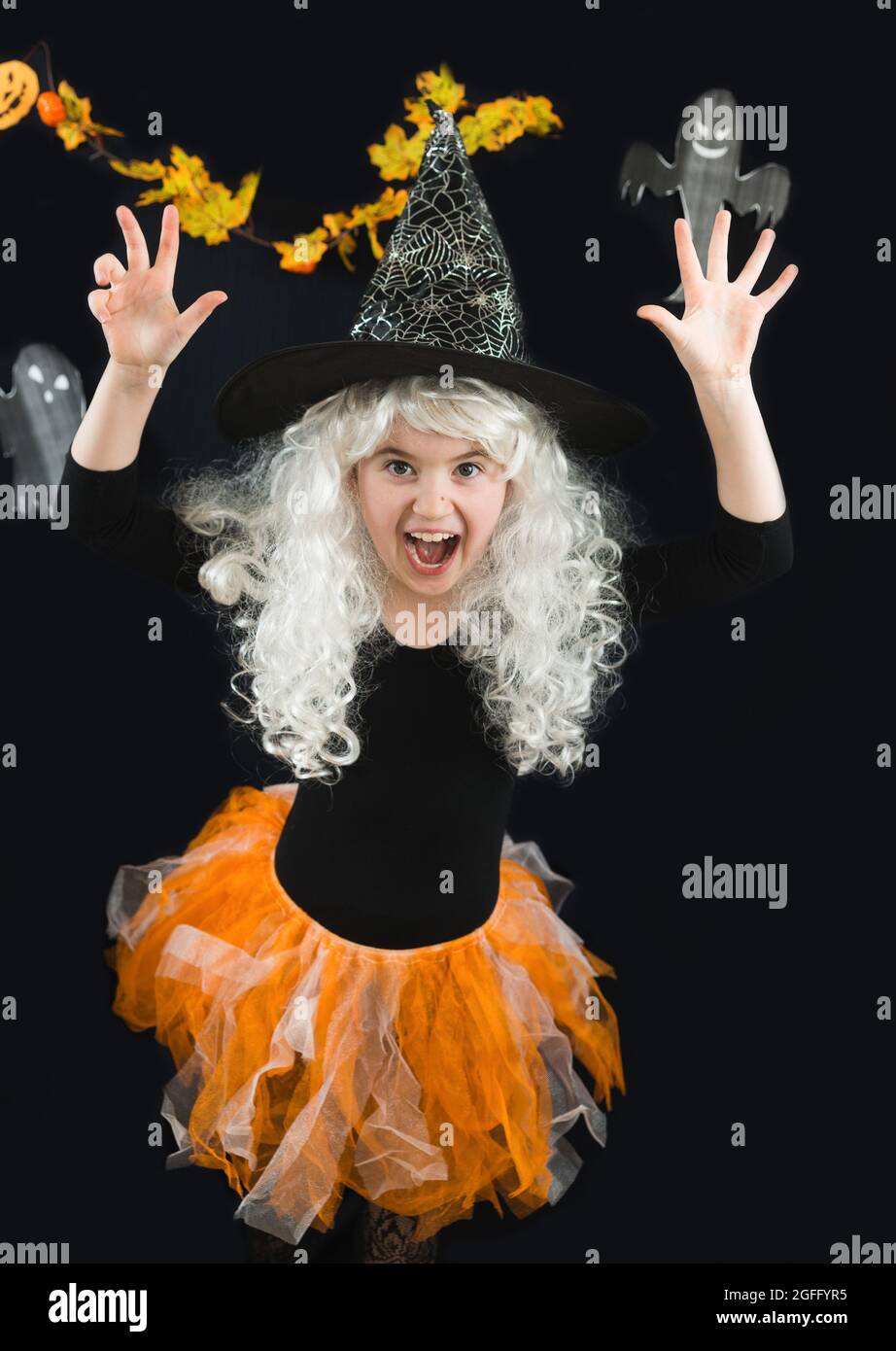Una ragazza allegra in una parrucca bianca e un costume strega spaventa. Orrore. Il fantasma di Casper è sullo sfondo Foto Stock