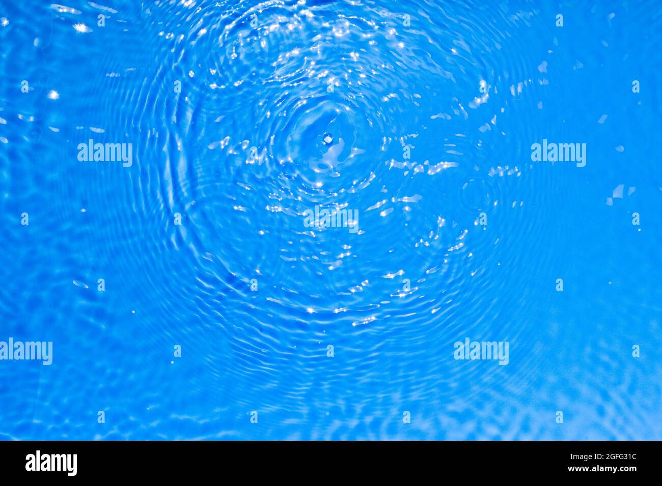 Superficie di blu trasparente piscina acqua texture con cerchi sull'acqua. Sfondo naturale astratto alla moda. Onde d'acqua alla luce del sole Foto Stock