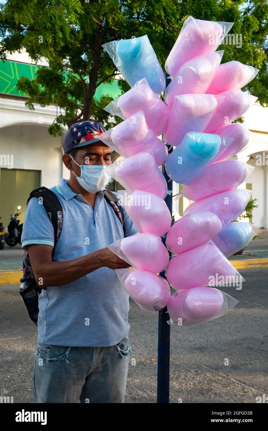 Riohacha, la Guajira, Colombia - Maggio 26 2021: L'uomo marrone latino con un cappuccio blu e usando una maschera Covid-19 sta vendendo la caramella di cotone nella strada Foto Stock