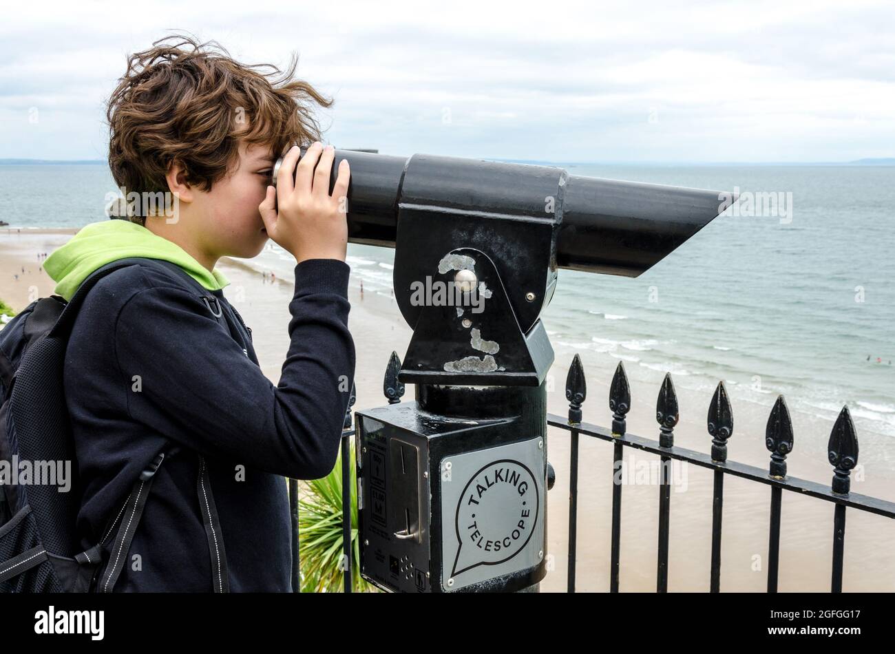 Un bambino usa un telescopio parlante sull'Esplanade a Tenby, Galles. Foto Stock