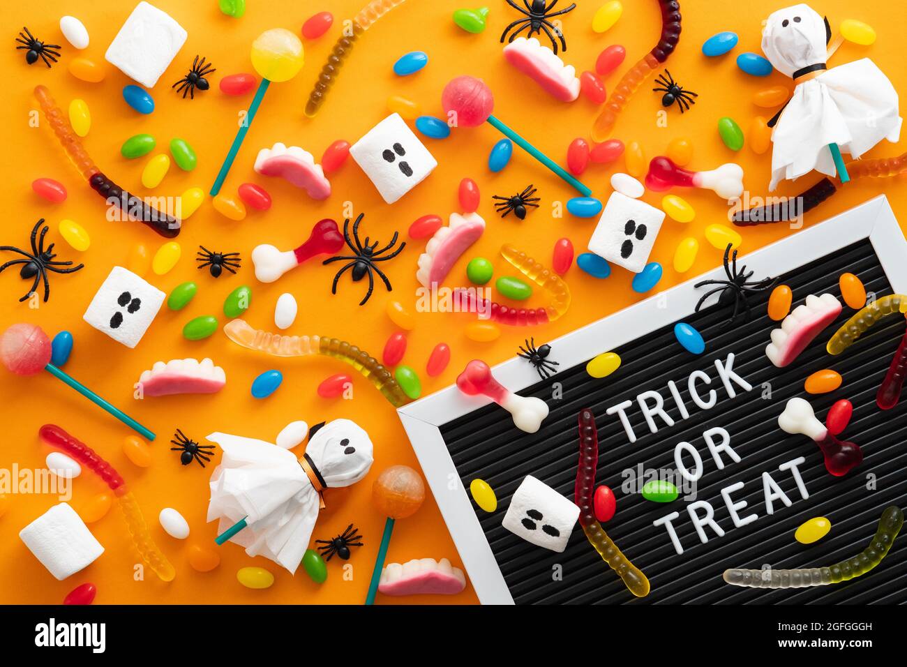 Felice Halloween concetto di vacanza. Caramelle e decorazioni di Halloween, letter board con testo Trick o trattare su sfondo arancione. Disposizione piatta, vista dall'alto, ov Foto Stock