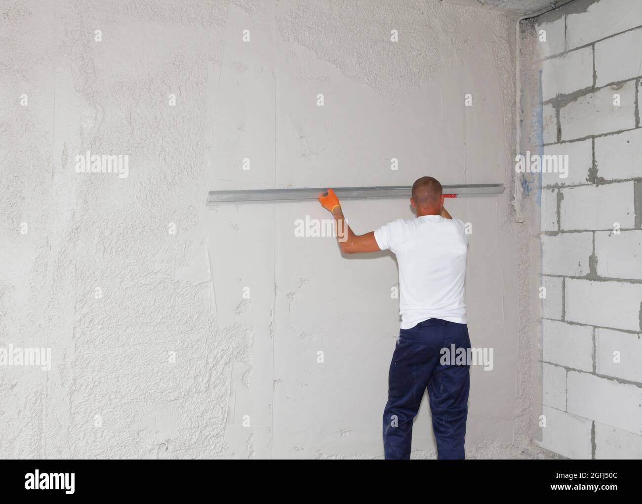 Un handyman, appaltatore di costruzione è rivestimento di skim, rifinendo, intonacando il drywall che rende il muro liscio con una lama larga e grande di skimming, knock-do Foto Stock