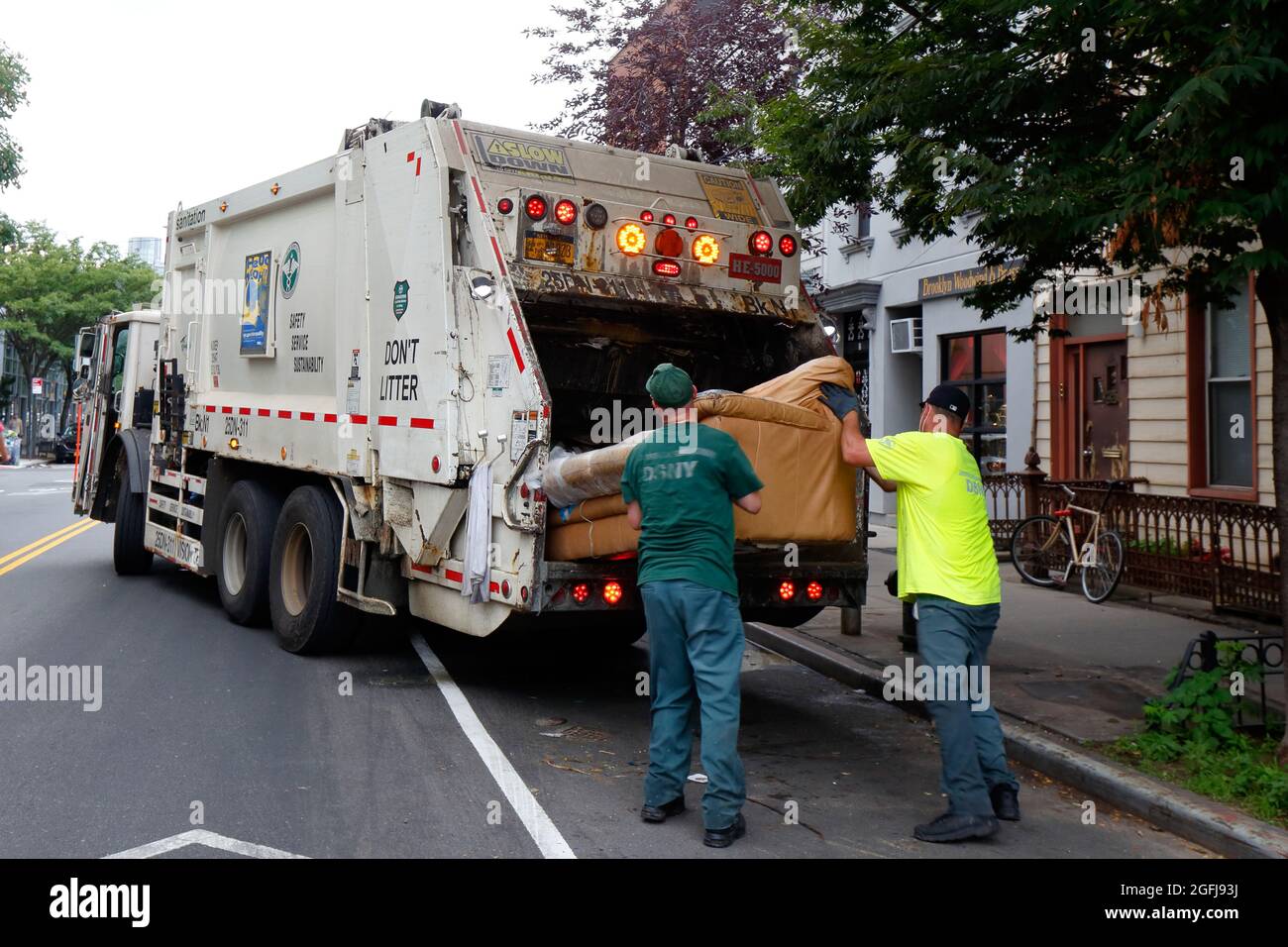 I lavoratori della sanificazione di NYC spingono un divano in un camion della spazzatura Foto Stock