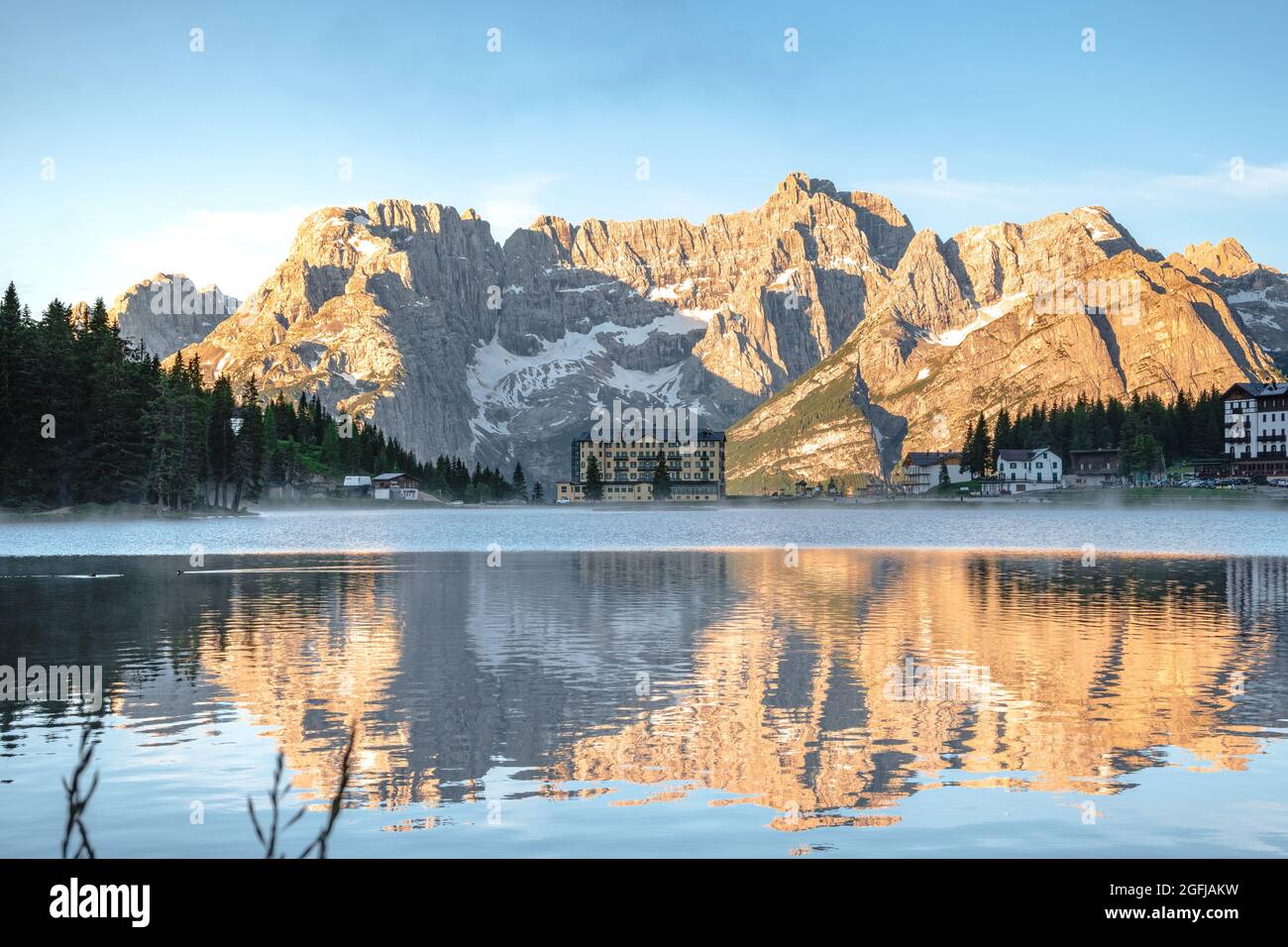 La tranquillità di un lago alpino subito dopo l'alba, le montagne dorate e la foschia sull'acqua. Lago di Misurina, Belluno, Veneto. Italia. Foto Stock