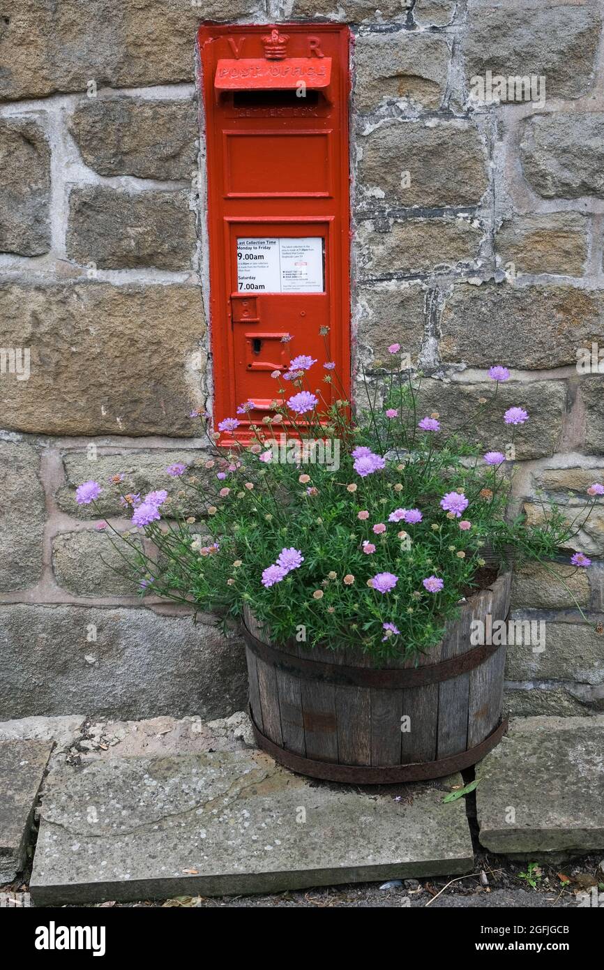 Una piccola casella di posta rossa posta in un muro di pietra e arricchito dalla vasca di legno di piante fiorite sotto. Foto Stock