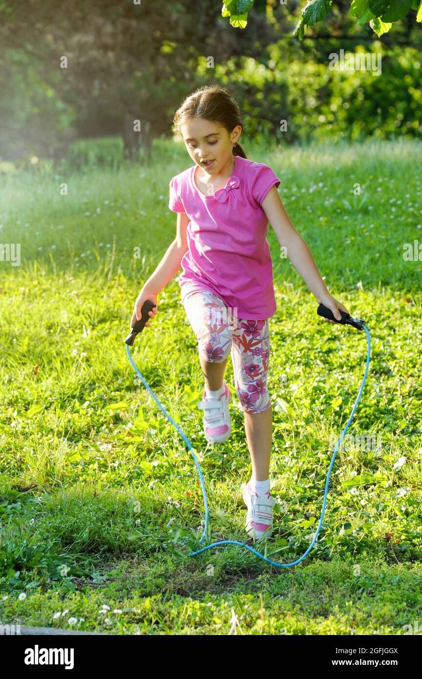 Giovane ragazza energica felice usando una corda saltando in un lussureggiante giardino verde in primavera o in estate in un sano stile di vita attivo all'aperto concetto Foto Stock