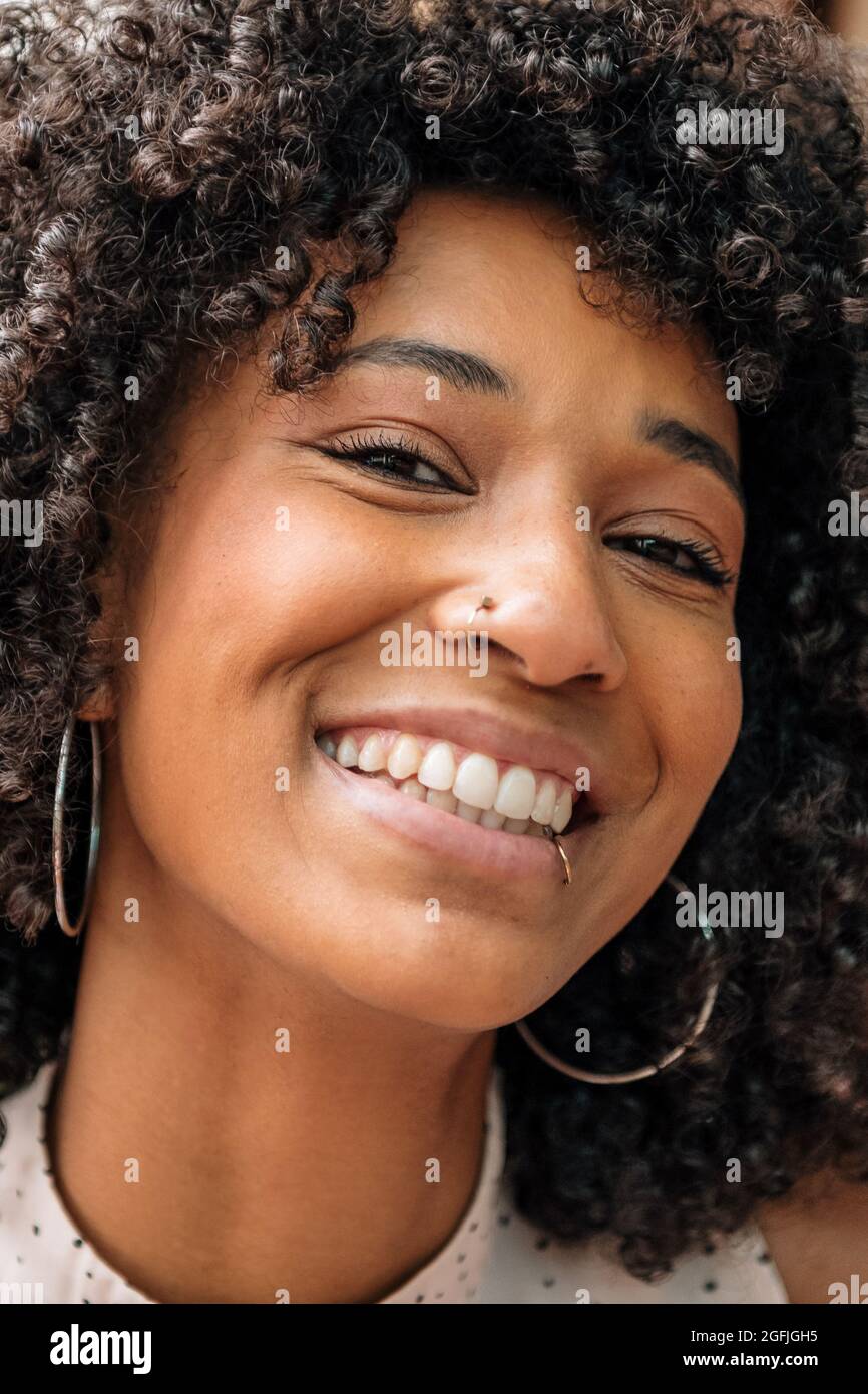 Ritratto di una bella donna nera sorridente amichevole con capelli ricci e piercing naso e labbro guardando la fotocamera con occhi ridenti in un primo piano Foto Stock