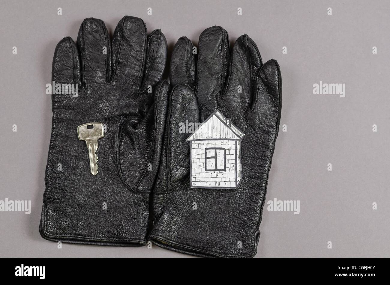 Casa di carta, chiave porta e guanti neri su sfondo grigio. Disegno su carta bianca di una casa con tetto, finestra e porta. Guanti in pelle. Vista dall'alto Foto Stock