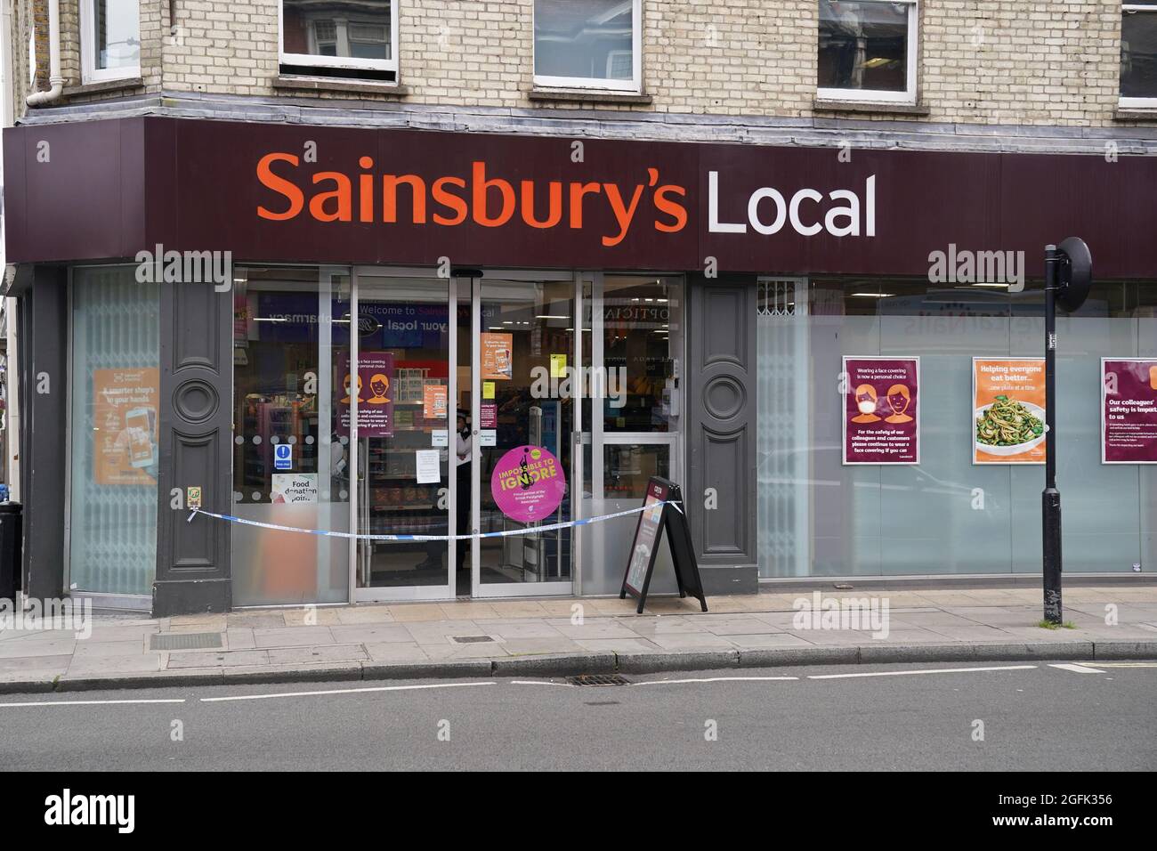 Nastro di polizia blocca l'ingresso alla locale di Sainsbury su Fulham Palace Road, West London, che è stato chiuso e una scena criminale messa in atto dopo che un uomo è stato arrestato per sospetto di contaminare il cibo con una siringa. Mercoledì sera la polizia è stata chiamata ad un uomo che gridava abusi alle persone in strada e tre supermercati Tesco Express, Little Waitrose e Sainsbury's Local - sono stati chiusi per indagini. Data foto: Giovedì 26 agosto 2021. Foto Stock