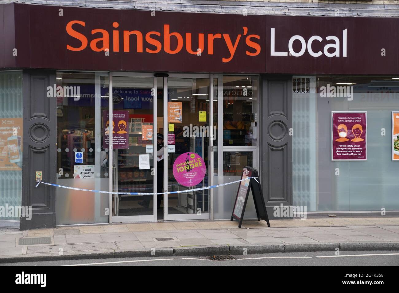 Nastro di polizia blocca l'ingresso alla locale di Sainsbury su Fulham Palace Road, West London, che è stato chiuso e una scena criminale messa in atto dopo che un uomo è stato arrestato per sospetto di contaminare il cibo con una siringa. Mercoledì sera la polizia è stata chiamata ad un uomo che gridava abusi alle persone in strada e tre supermercati Tesco Express, Little Waitrose e Sainsbury's Local - sono stati chiusi per indagini. Data foto: Giovedì 26 agosto 2021. Foto Stock