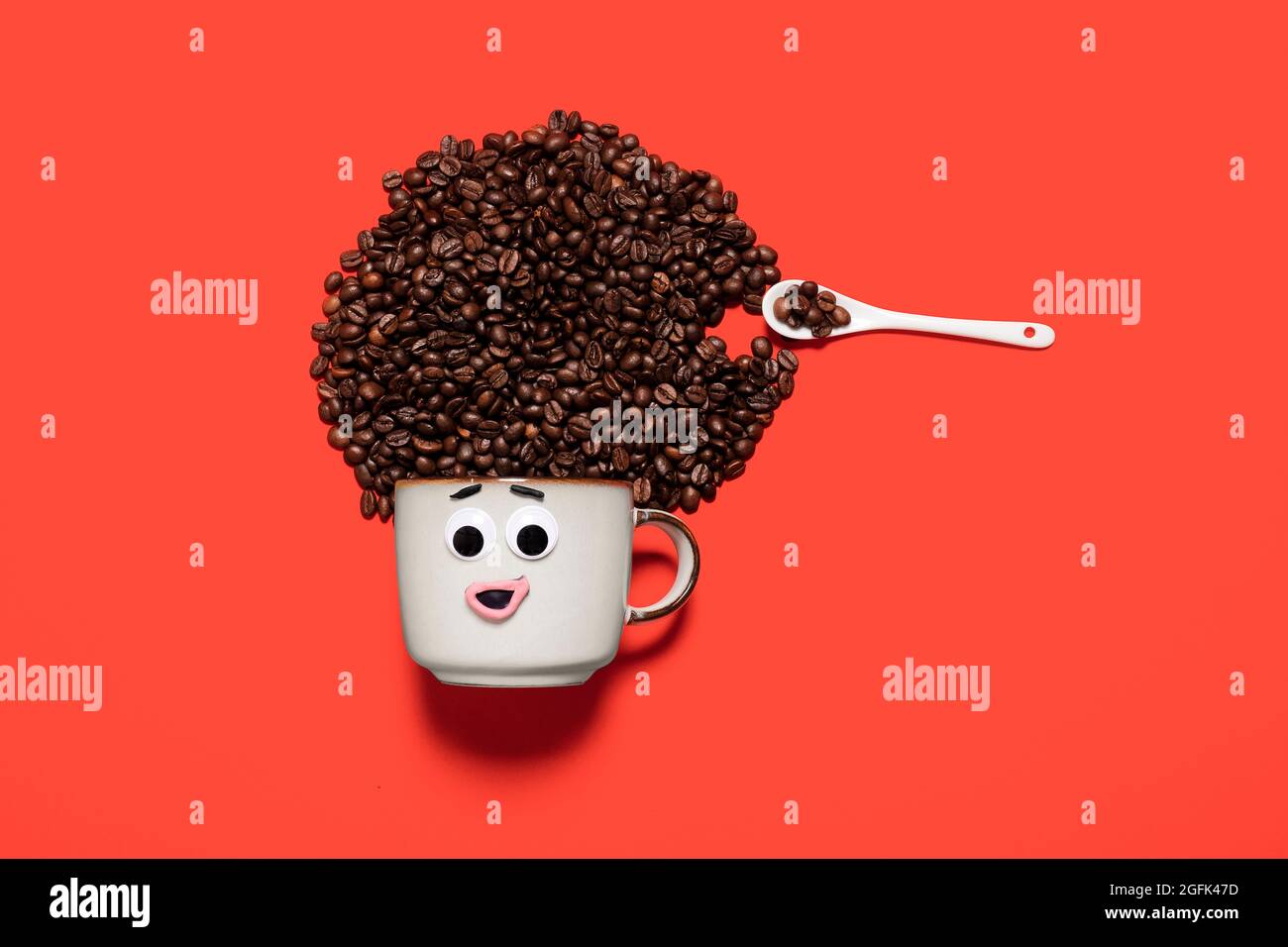 Tazza di caffè con occhi google e una bocca che forma un'espressione facciale con chicchi di caffè per capelli su sfondo rosso con spazio di copia e spazio per il testo. Foto Stock