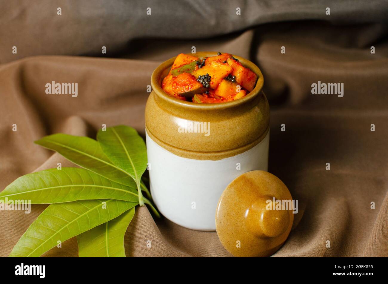 Sottaceti di mango crudi fatti in casa in un tradizionale vaso in ceramica su sfondo marrone Foto Stock