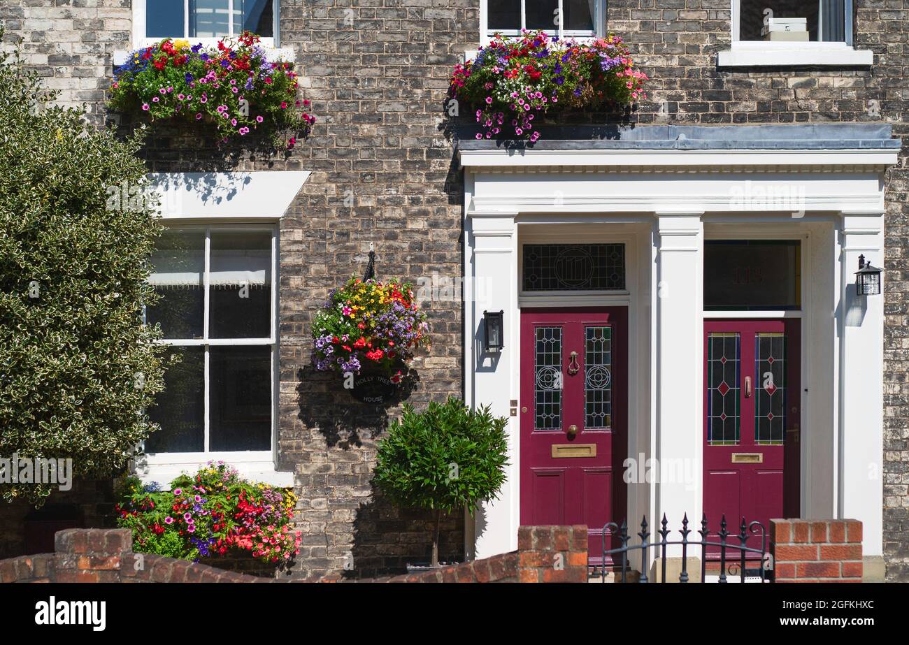 Vista frontale della tradizionale casa a schiera con finestre a telaio e cesti pendenti con fiori in piena fioritura la mattina d'estate. Beverley, Regno Unito. Foto Stock