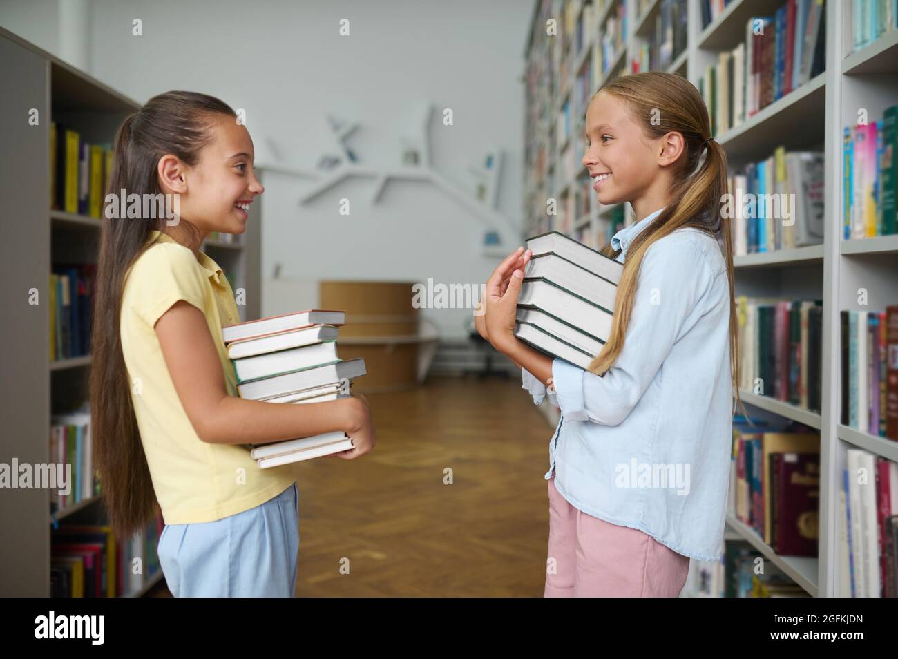 Due scolari allegri che tengono in mano mucchi di libri Foto Stock