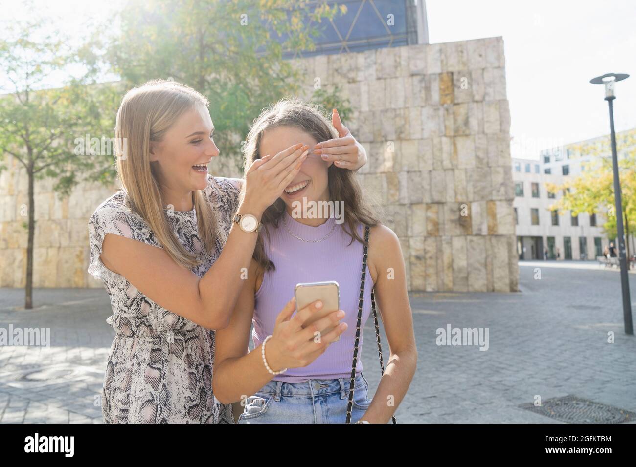 La ragazza sorprende la ragazza e copre i suoi occhi in città Foto Stock