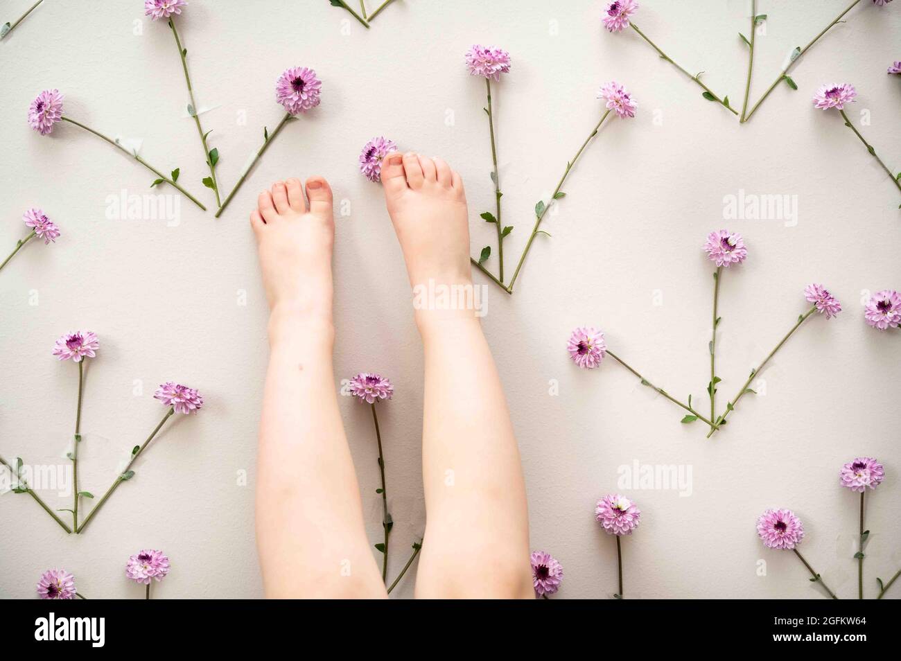 I piedi piccoli del toddler contro una parete dei fiori viola Foto Stock