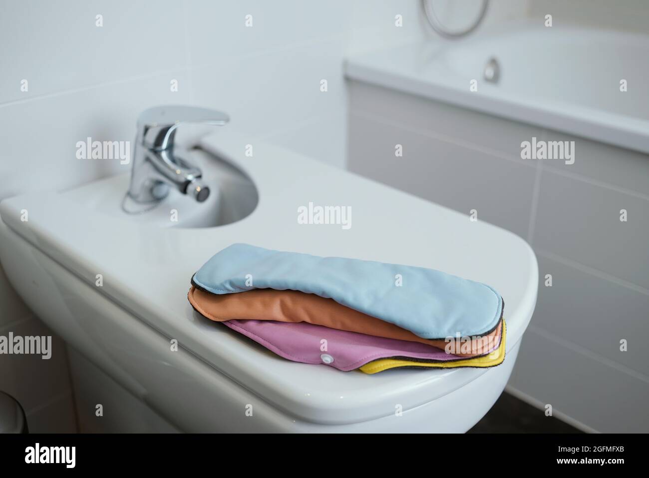 alcuni panni mestruali di diversi colori sul coperchio di un bidet bianco in un bagno moderno Foto Stock
