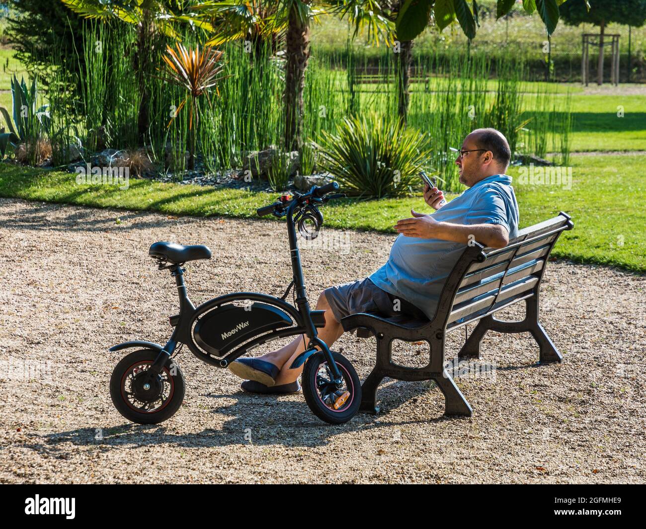 Uomo con bicicletta elettrica, parlando al telefono in giardino pubblico - Loches, Indre-et-Loire (37), Francia. Foto Stock