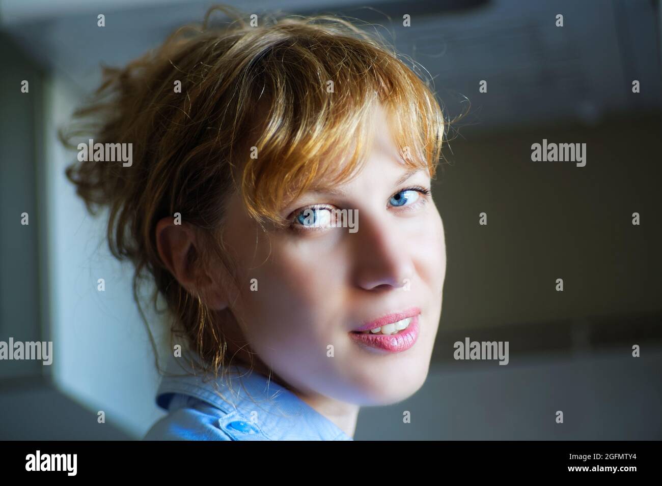 La ragazza con occhi blu con capelli rossi guarda la fotocamera a metà giro. Messa a fuoco soft. Sfondo sfocato. Foto Stock