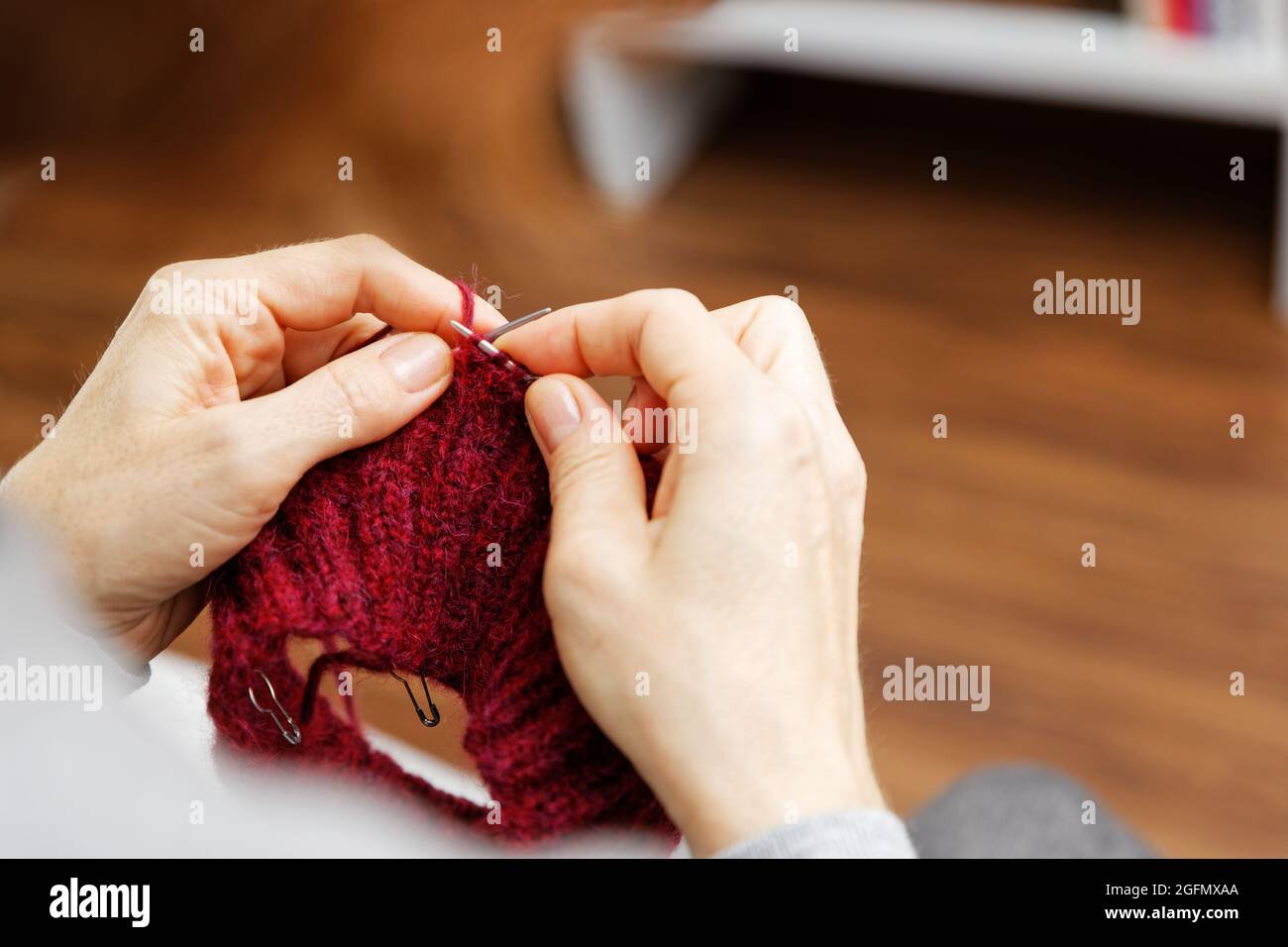 Closeup womans mani maglia rosso filato di lana borgogna con aghi di maglia.  Vista dall'alto. Messa a fuoco superficiale Foto stock - Alamy