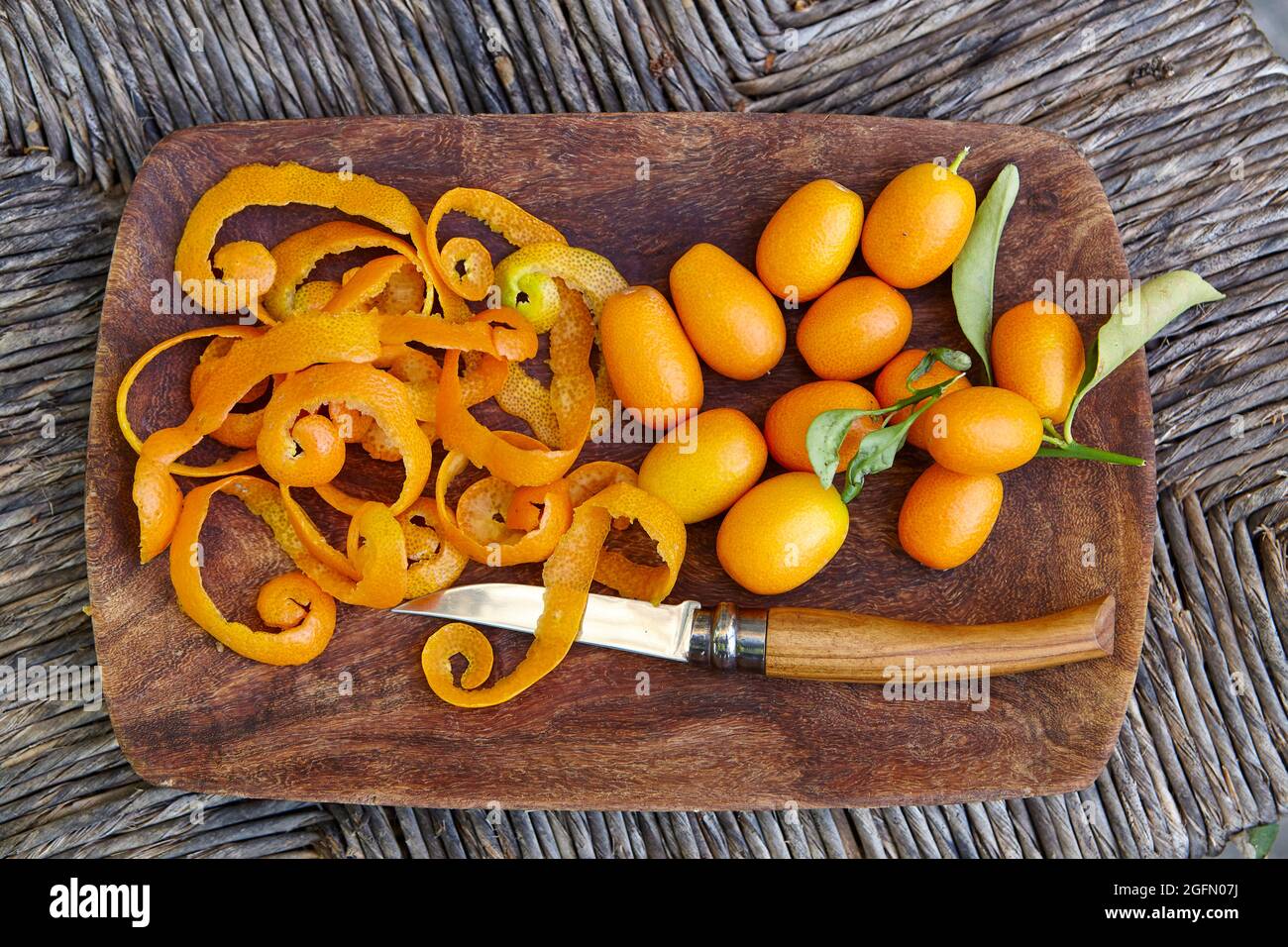 Mostra di kumquat appena raccolti, buccia di kumquat e un coltello di frutta in una ciotola di legno Foto Stock