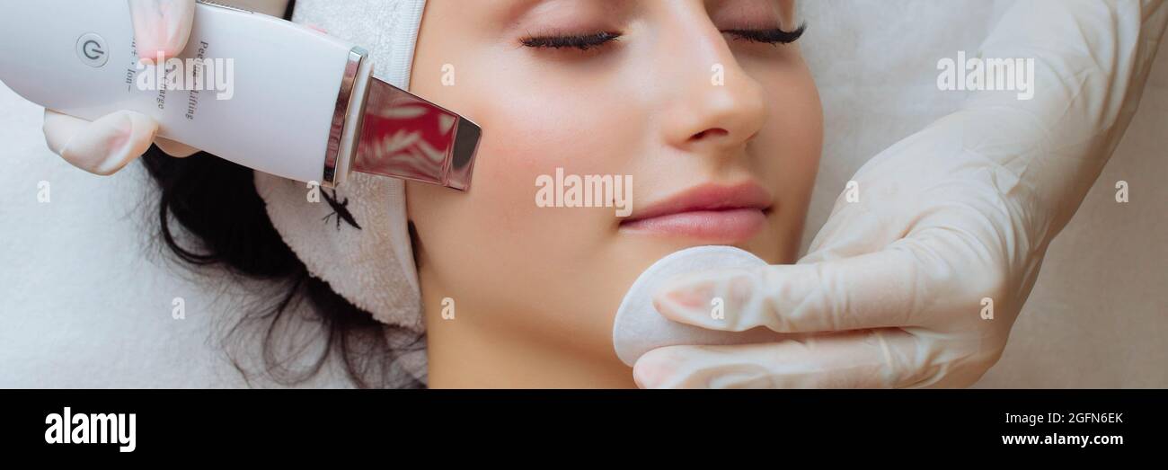 Striscione di giovane donna caucasica durante la procedura di pulizia della pelle con ecografo. Dispositivo a ultrasuoni nelle mani di Foto Stock