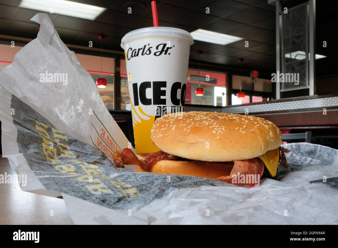 Un panino Western Bacon Cheeseburger su un involucro aperto e una tazza di bibite analcoliche con una paglia rossa in un ristorante fast food Carl's Junior. Foto Stock