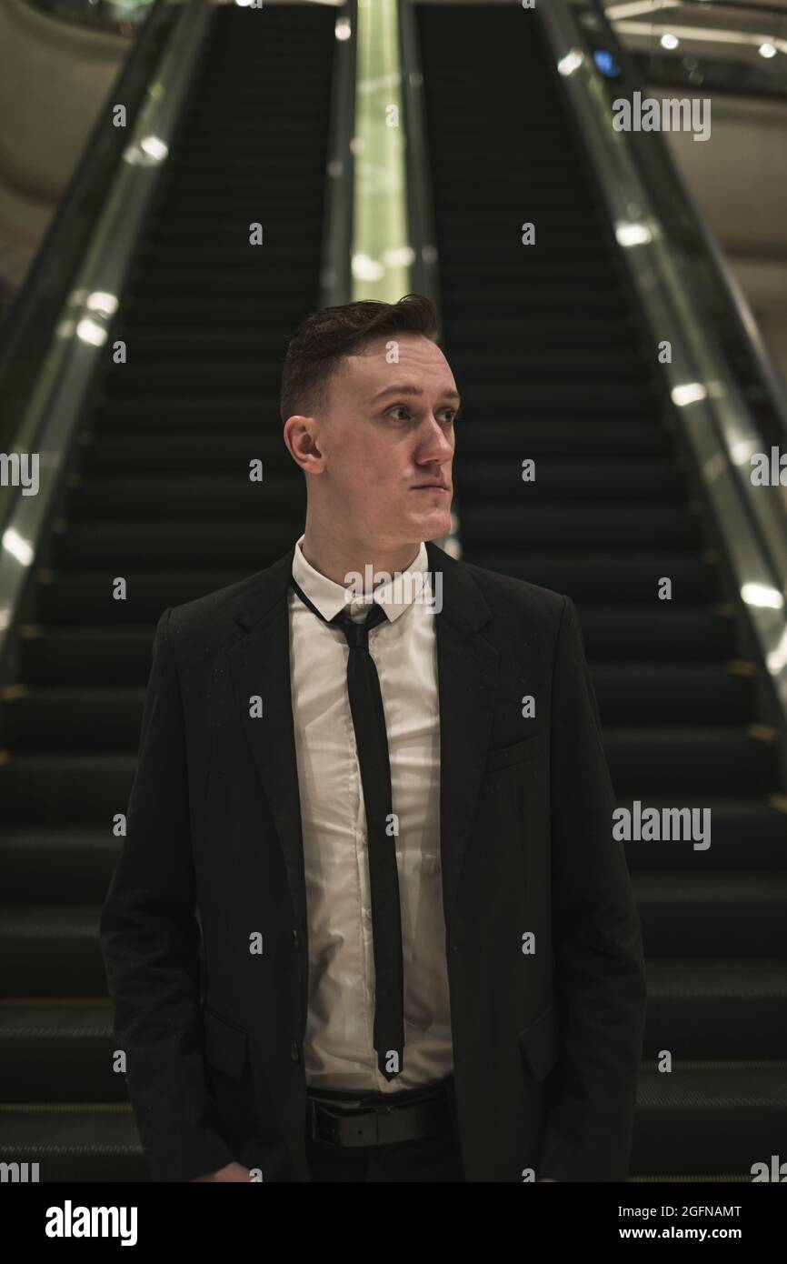 Ritratto di giovane bel uomo d'affari caucasico in elegante abito da affari con la cravatta si erge vicino alla scala mobile. Foto Stock
