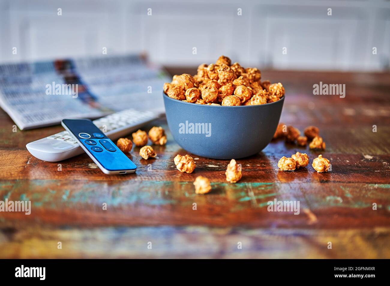 Tavolo in legno con snack, telecomando e quotidiano televisivo. Foto Stock